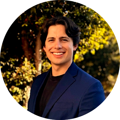 jay-headshot Person in blue blazer smiling outdoors with trees in the background.